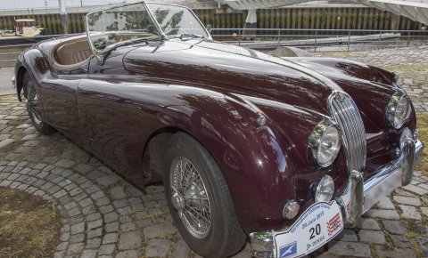 Dunkelroter Oldtimer von Jaguar vor einem Hafenbecken.